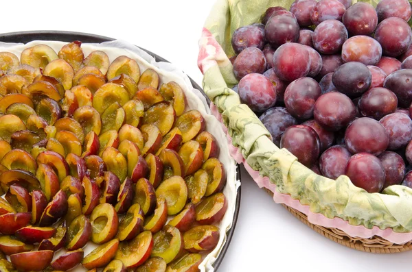 Plum tart before baking and a basket with fresh plums — Stock Photo, Image