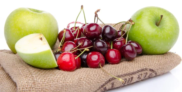 Спелые зеленые яблоки и красные вишни на мешковине — стоковое фото