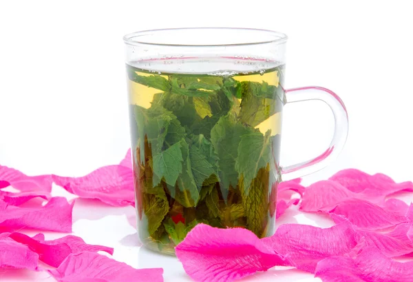 Cup of mint tea surrounded with pink petals — Stock Photo, Image