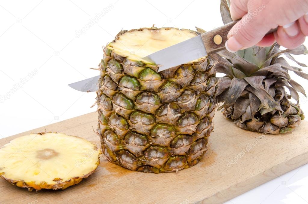 Hand peeling a pineapple on a wooden board