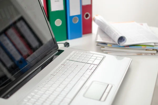 Laptop op een bureau met bindmiddelen en tijdschriften — Stockfoto