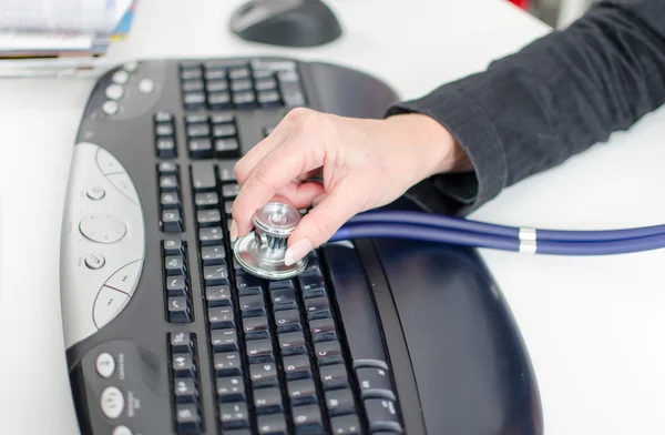 Mano de mujer revisando un teclado con un estetoscopio — Foto de Stock