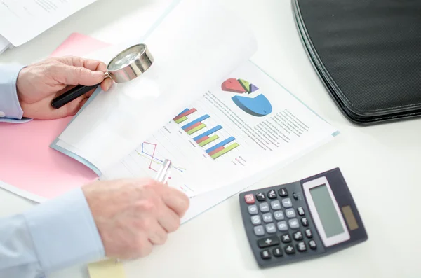 Empresario revisando un gráfico con una lupa — Foto de Stock