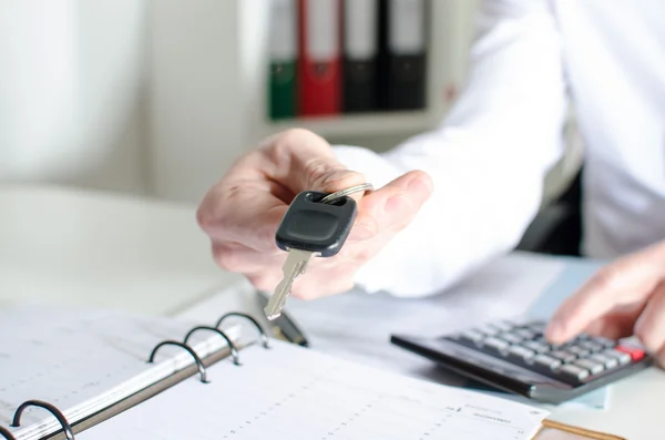 Car salesman holding a key and calculating a price — Stock Photo, Image