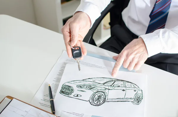 Car salesman showing a key and a car design — Stock Photo, Image