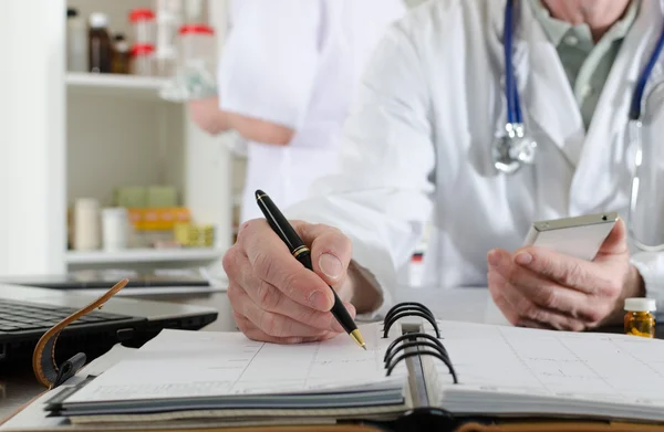 Doctor holding a smartphone and taking notes — Stock Photo, Image