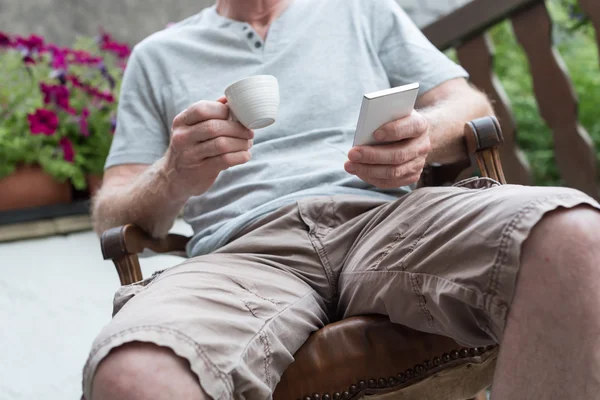 Uomo usando il suo smartphone e tenendo in mano una tazza di caffè — Foto Stock