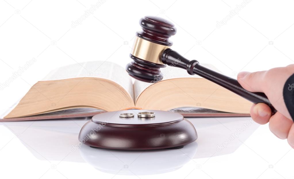 Hand holding a judge gavel above wedding rings
