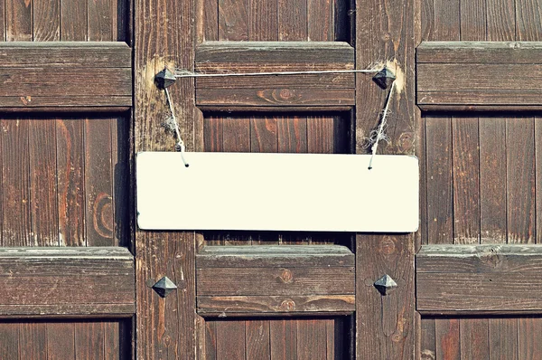 Blank white sign hanging with old rope on the weathered brown wooden wall with metal rivets - retro tones background