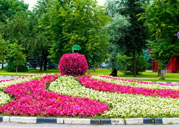 Street landscaping in cloudy day - flowerbed with landscaping element in form of big apple covered with pink begonia flowers.