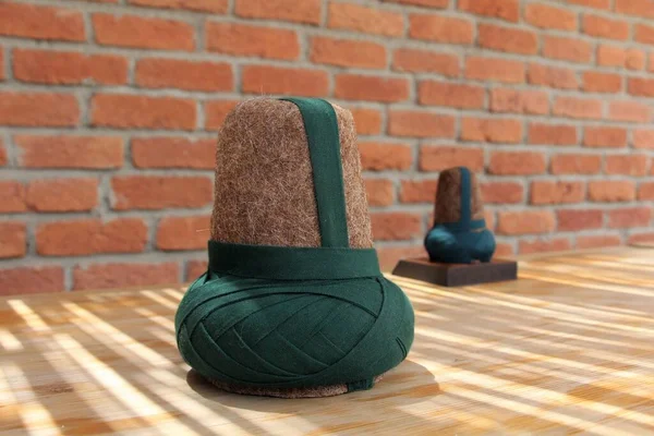 A hat made of felt worn by the whirling dervishes. The brown hat worn by the Mevlevi dervishes. There is a brick wall in the background.