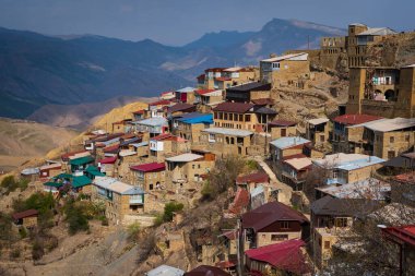 Köy Dağıstan dağlarında, çatılar parlak güneşle aydınlanıyor, dağlar ve vadilerin zirveleri arka planda..