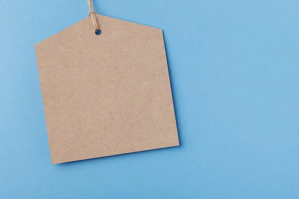 Prázdný hnědý papírový štítek svázaný provázkem. cenovka na modrém pozadí — Stock fotografie