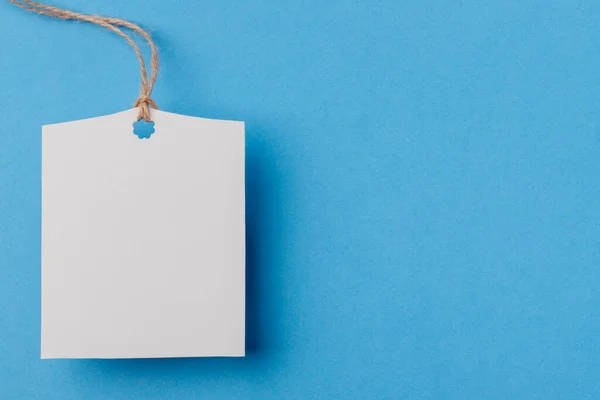 empty white rectangular paper tag on a rope on blue background