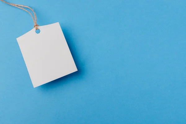 empty white rectangular paper tag on a rope on blue background