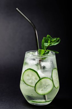 Salatalık ve naneli limonata siyah masa zemininde metal tüplü bir bardakta.