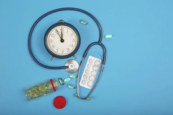 Time to take your pills. Pills, stethoscope and alarm clock on a blue background. Top view.