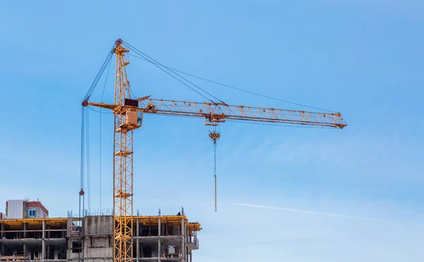 Construction cranes and unfinished apartment building against the blue sky. Housing construction.