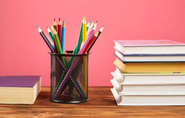 Bir yığın kitap, pembe arka planda renkli kalemler..