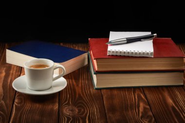 Kitap yığını, not defteri, bir fincan espresso kahve ve koyu arkaplanda bir kalem..