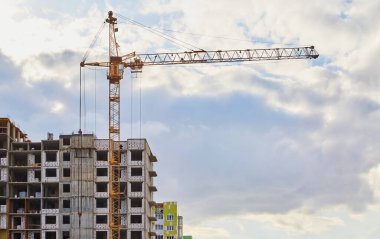 İnşaat vinci ve bitmemiş iskan binası bulutlu gökyüzüne karşı.