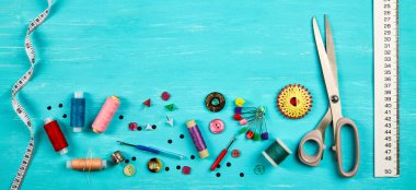 Mavi bir masaya aksesuar dikiyorum. Dikiş iplikleri, iğneler, iğneler, düğmeler, makas, dikiş santimetresi ve kesicinin mezurası. Boşluğu kopyala.