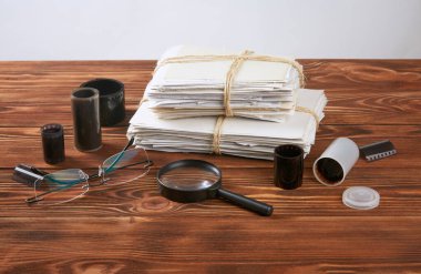 Bir yığın eski fotoğraf, gözlük, büyüteç ve negatifler ahşap bir masanın üzerinde..