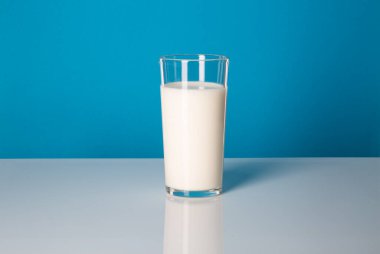 Süt ve mayalanmış süt ürünleri: vücuda yarar sağlar. Mavi arka planda bir bardak süt..