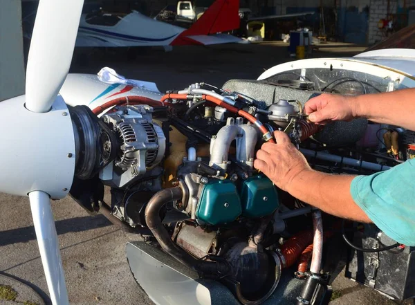 Carrying out engine maintenance on a light aircraft, showing the engine, propeller, hangar and other aircraft.