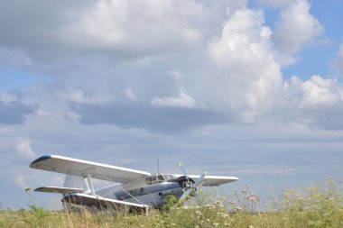 AN-2 uçağı, hava sahasında, bulutlu mavi bir gökyüzünün arka planında tasvir edilir.