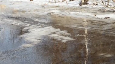 Karı, ağaçları, akmakta olan bir nehri gözlemleriz..