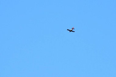 Büyük mavi bir yay gökyüzünün arka planında uçan bir uçak görüyoruz.