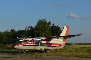 Hafif bir çift motorlu turboprop uçak yeşil ağaçlı ve arka planda mavi gökyüzü olan bir havaalanına park edilmiş..