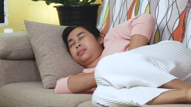 亚洲女人手牵着肚子 在家里沙发上休息 感觉月经疼痛或胃炎 — 图库视频影像