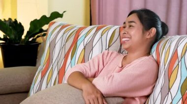 Evde oturma odasındaki kanepede televizyon izlerken akıllı telefondan konuşan rahat genç bir kadın. Kadınların elektrikli aletlerle evde zaman geçirmesi fikri..