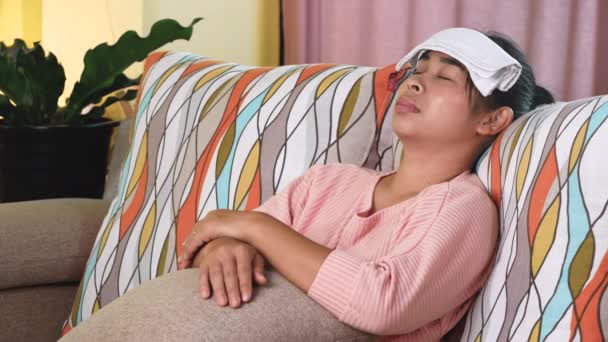 病気の女性は家のソファの上に横たわる熱頭痛を緩和するために彼女の額にぬれたタオルを置いた — ストック動画
