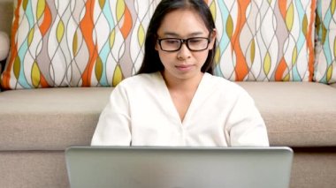 Gözlük takan yorgun bir kadın, ofiste dizüstü bilgisayarla çalışırken rahatlamak için kollarını uzatıyor..