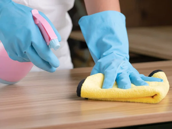 Eldiven giymiş, ev işi yapan, evde masasında sprey deterjan bulunan bez kullanan genç bir ev kadınının fotoğrafını çek. Ev işi kavramı.