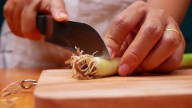 Japon Uzun Soğanı, Japon Scallion 'u ya da tahta kesme tahtasındaki Yeşil Soğan' ı kesmek için mutfak bıçağı kullanan bir kadın. Kadın mutfakta yemek hazırlıyor. Yemek pişirme konsepti.
