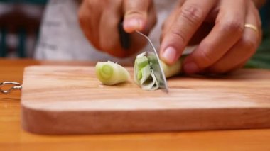 Japon Uzun Soğanı, Japon Scallion 'u ya da tahta kesme tahtasındaki Yeşil Soğan' ı kesmek için mutfak bıçağı kullanan bir kadın. Kadın mutfakta yemek hazırlıyor. Yemek pişirme konsepti.