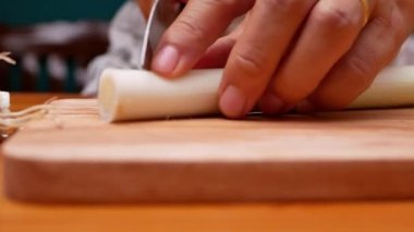 Japon Uzun Soğanı, Japon Scallion 'u ya da tahta kesme tahtasındaki Yeşil Soğan' ı kesmek için mutfak bıçağı kullanan bir kadın. Kadın mutfakta yemek hazırlıyor. Yemek pişirme konsepti.