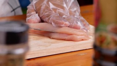 Eldivenli kadın, evde lezzetli yemekler hazırlamak için tahta kesme tahtasıyla tavuk kesiyor. Ev yapımı pişirme konsepti.