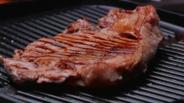 Izgara tabakta baharat ve otlarla sulu biftek kızartıyorum ve yavaş çekimde duman yükseliyor. Sağlıklı gıda konsepti.