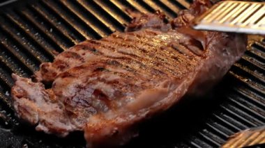 Izgara tabakta baharat ve otlarla sulu biftek kızartıyorum ve yavaş çekimde duman yükseliyor. Sağlıklı gıda konsepti.