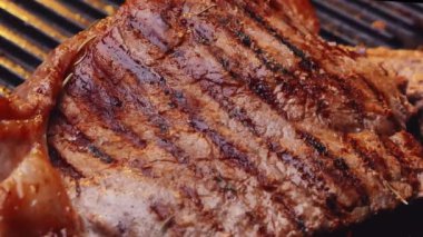Izgara tabakta baharat ve otlarla sulu biftek kızartıyorum ve yavaş çekimde duman yükseliyor. Sağlıklı gıda konsepti.