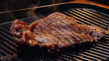 Izgara tabakta baharat ve otlarla sulu biftek kızartıyorum ve yavaş çekimde duman yükseliyor. Sağlıklı gıda konsepti.