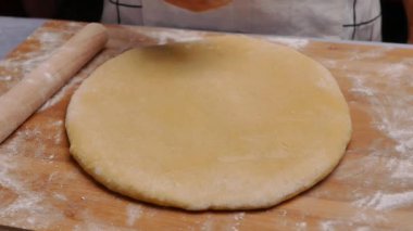Un içindeki kadın eller hamuru ahşap bir masanın üzerinde yuvarlar hamuru pizza ya da çörek yapmak için hazırlar. Yemek pişirme süreci.
