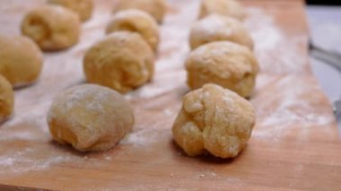 Kadın eli hamurdan bir parça keser ve ahşap bir masada donut yapmak ve un serpiştirmek için toplar oluşturur. Yemek pişirme süreci.