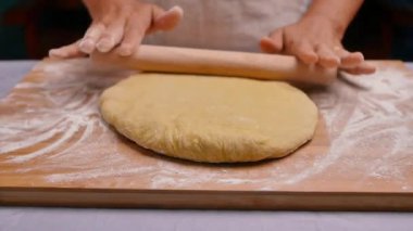 Un içindeki kadın eller hamuru ahşap bir masanın üzerinde yuvarlar hamuru pizza ya da çörek yapmak için hazırlar. Yemek pişirme süreci.