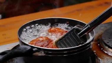 Tavuk budu kızartıyorum. Mutfak ocağında tavada sıcak yağda. Tavuk butlarını kızgın yağda döndürmek için mutfak maşası kullanan kadın eller. Sağlıksız Yemek.